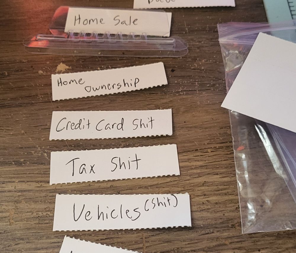 Hanging folder labels on a desk: home ownership,  credit card shit, tax shit, vehicles (shit)