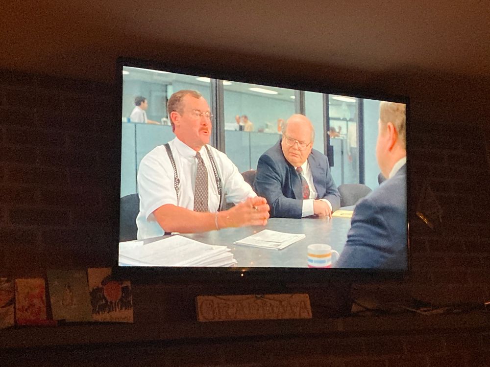 A scene from office space on the tv. Two bobs sitting in a conference room
