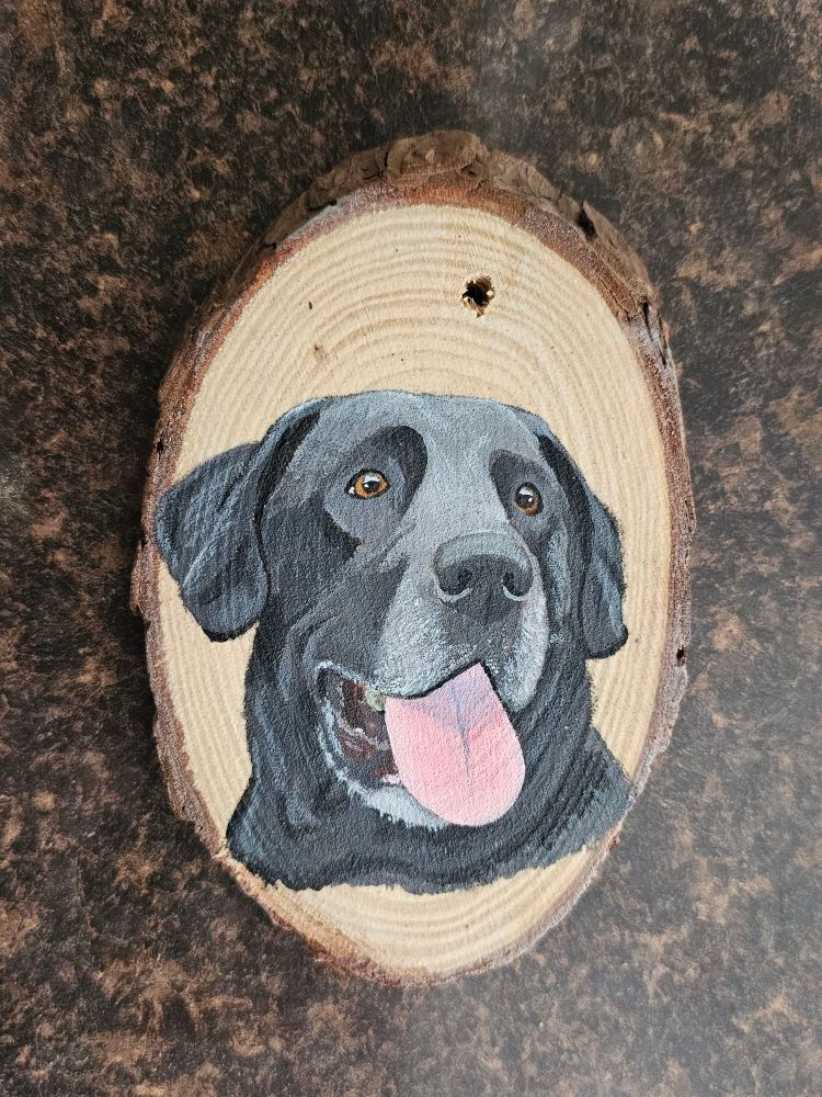 An acrylic pet portrait painting of a black labrador on a wood slice ornament.