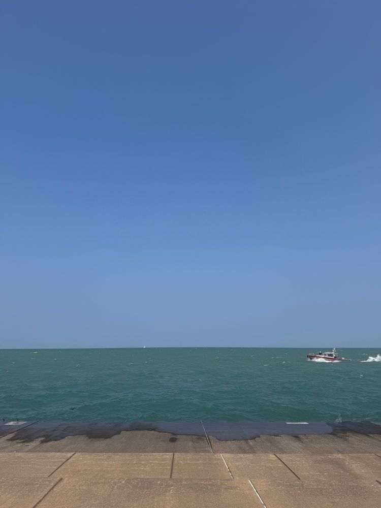 Picture of the concrete beach and Lake Michigan. Coast guard ship is entering frame right. Blue skies and blue water. 