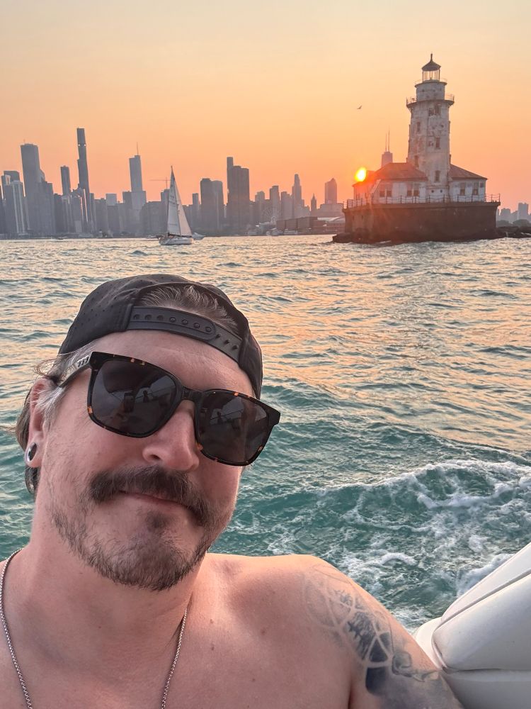 A sunset selfie of me with the Chicago skyline, a sailboat, and a light house. Taken from a boat on Lake Michigan. 