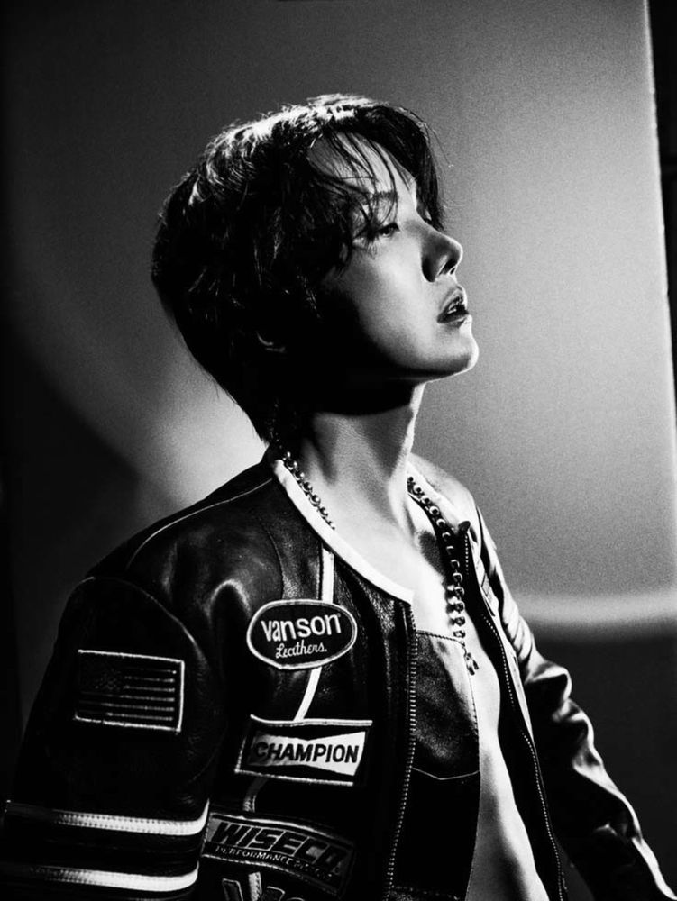 a black and white image of hoseok in profile with his eyes mostly closed and his lips barely parted. he is not wearing a shirt, but he does have a bulky racer type jacket on