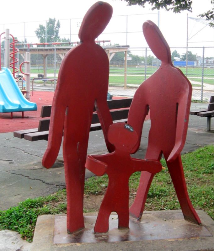 Small people standing on a flat square concrete square..  
Two adult figures and one child.  
All flat bent red metal 