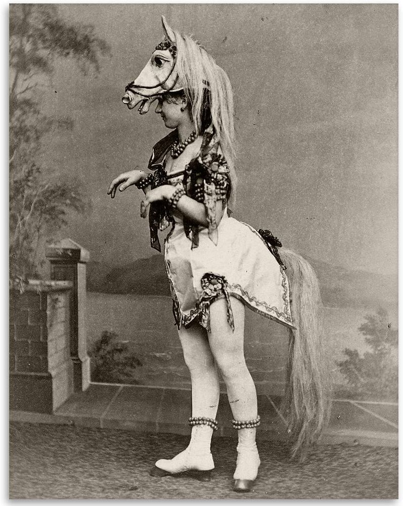 An early 20th century photograph of a chorus girl in a horse costume. She is wearing a horse head headpiece, her bustle has a horse tail attached to it, and her shoes have hooves at the toes.