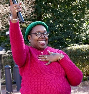 Lauren 'Bemi' Byrd, Transportation Community Organizer at No Boundaries Coalition, stands proudly holding a microphone up high after sharing her thoughts about transit in Baltimore.