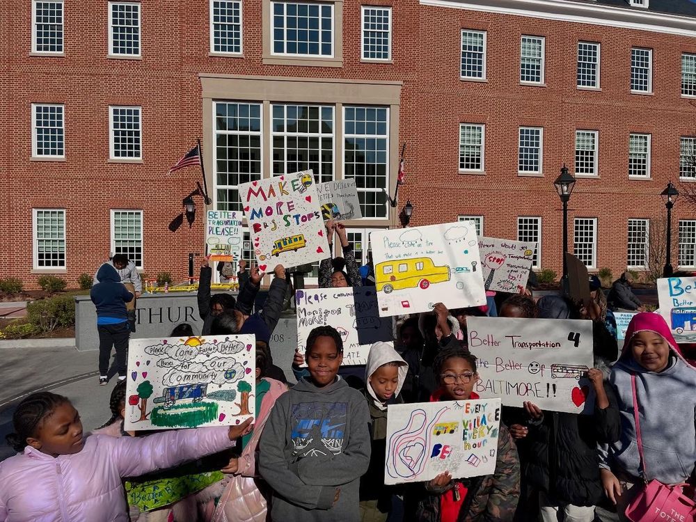 A photo taken during the Transit Riders Rally on February 4th outside the Maryland State House in Annapolis of elementary school kids holding signs asking for better transit service in Baltimore so that they can get to school on time.