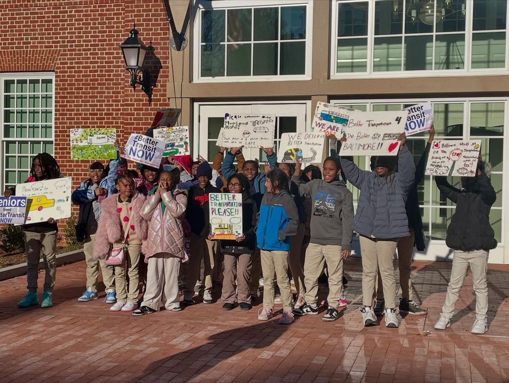 A photo taken during the Transit Riders Rally on February 4th outside the Maryland State House in Annapolis of elementary school kids holding signs asking for better transit service in Baltimore so that they can get to school on time.