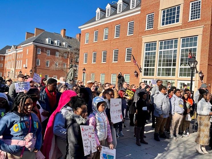 A photo taken during the Transit Riders Rally on February 4th outside the Maryland State House in Annapolis of elementary school kids holding signs asking for better transit service in Baltimore so that they can get to school on time.