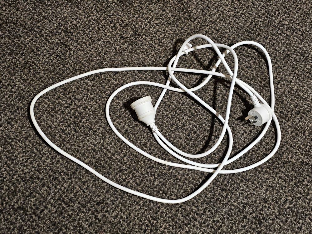 White electrical power extension cord on brown speckled carpet.