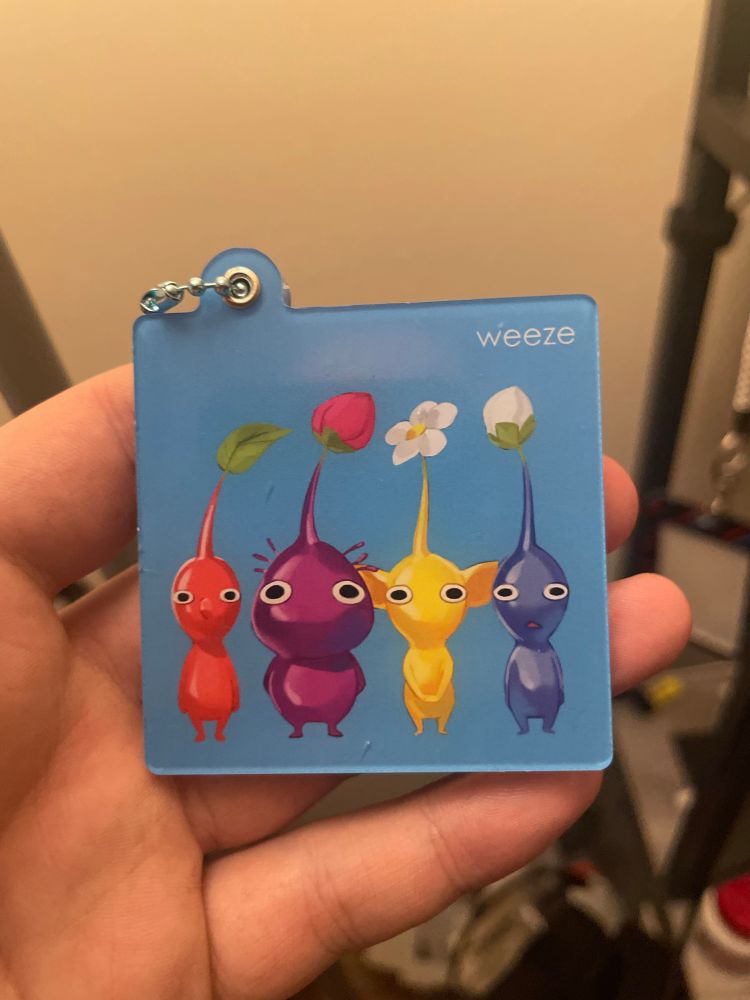 Picture of me holding a keychain/charm with Pikmin on it in the pose of Weezer's Blue Album with the text saying weeze