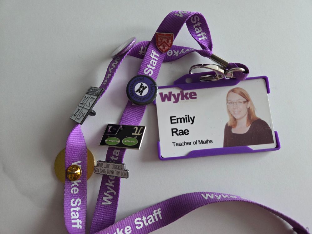 An ID badge on a purple lanyard. The badge has a photo of me, with my name and Teacher of Maths. There are assorted items of lanyard bling along the length of it - mainly pin badges with silly maths jokes and a pin from my university reunion (Collingwood College, Durham)