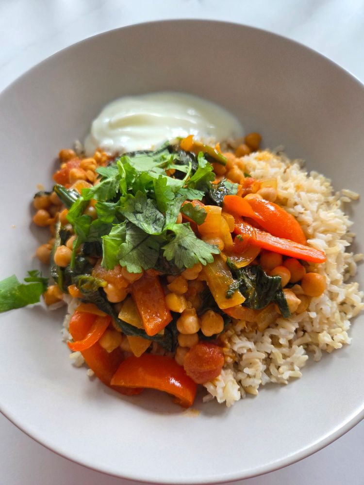A portion of Brazilian chickpea curry in a cream coloured pasta bowl, with rice, yoghurt and (maybe controversially) coriander 
