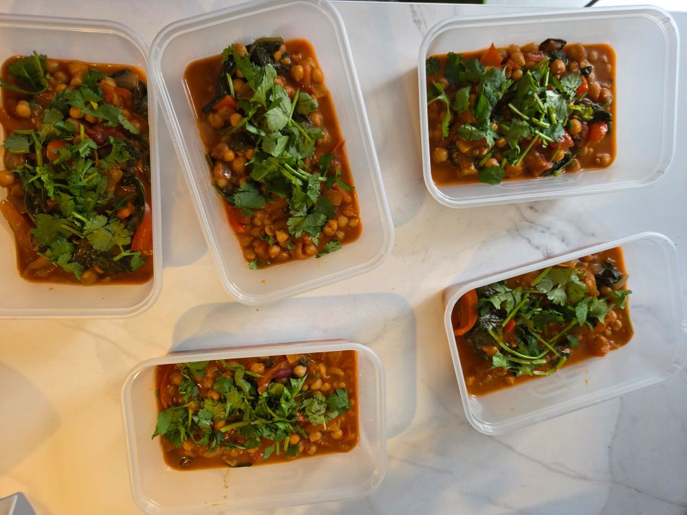 Five takeaway containers filled with meal prepped portions of the same curry, to be frozen