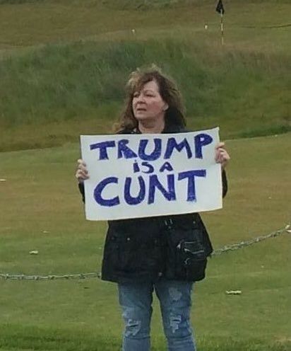 Photo of Janey Godley holding a notice which says Trump is a cunt.