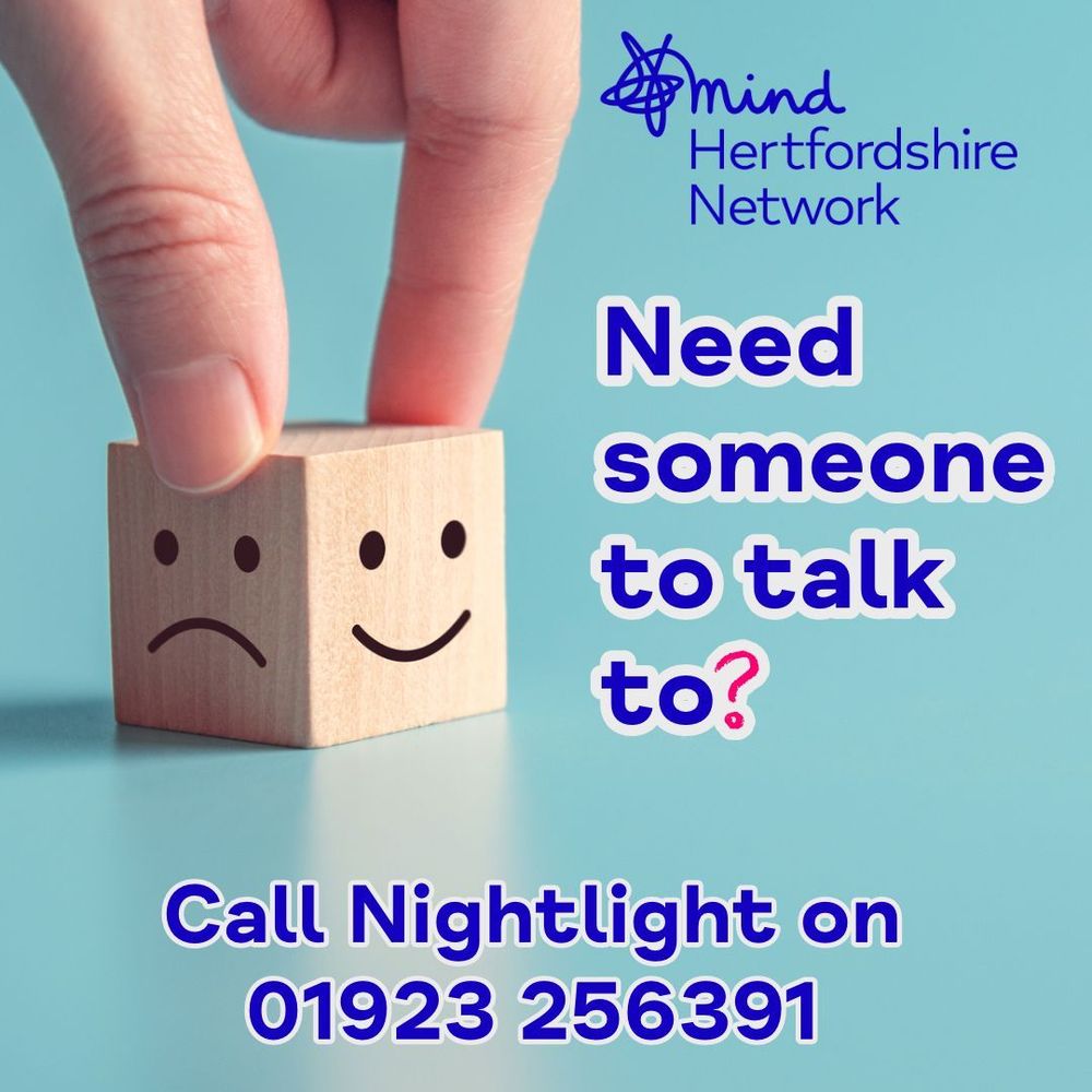 A wooden block with a sad face is being turned to show a happy face. The background is light blue. The text reads, “Need someone to talk to? Call Nightlight on 01923 256391,”. The Hertfordshire Mind Network logo is in the top right corner