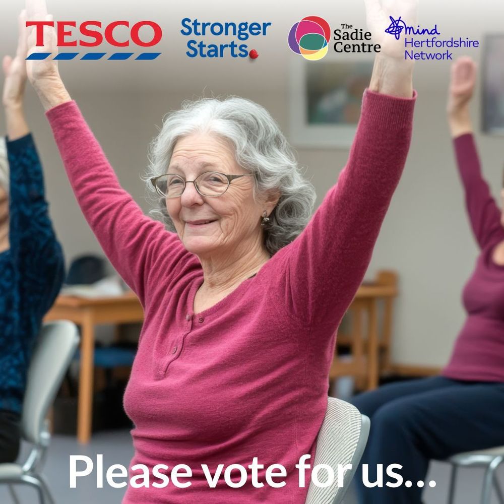 An older woman with grey hair and glasses smiles while raising both arms in a seated exercise class. She is wearing a pink top. Logos for Tesco, Stronger Starts, The Sadie Centre, and Mind Hertfordshire Network appear at the top of the image. The text at the bottom reads, “Please vote for us…”