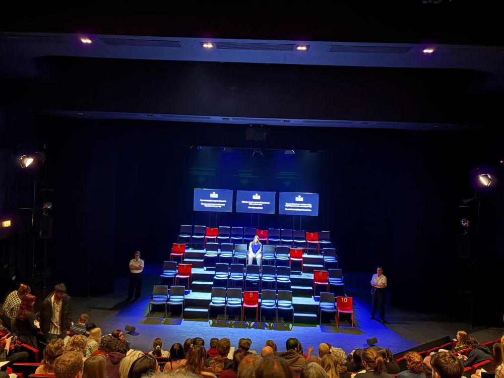 Photo of the set for a stage play, with a full audience watching