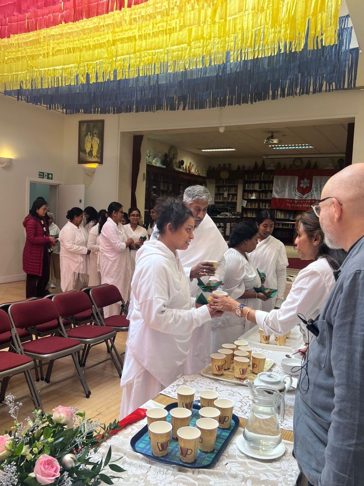 Buddhist lay devotees, dressed in white, queue at a table from which they are served tea or coffee, and butter cake