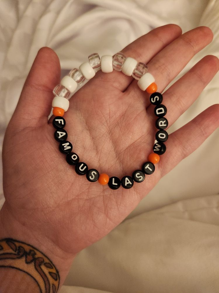 photo of me holding a bracelet that spells out "famous last words". thr bracelet is made of red, white, and clear beads with the letters being black beads with white writing.