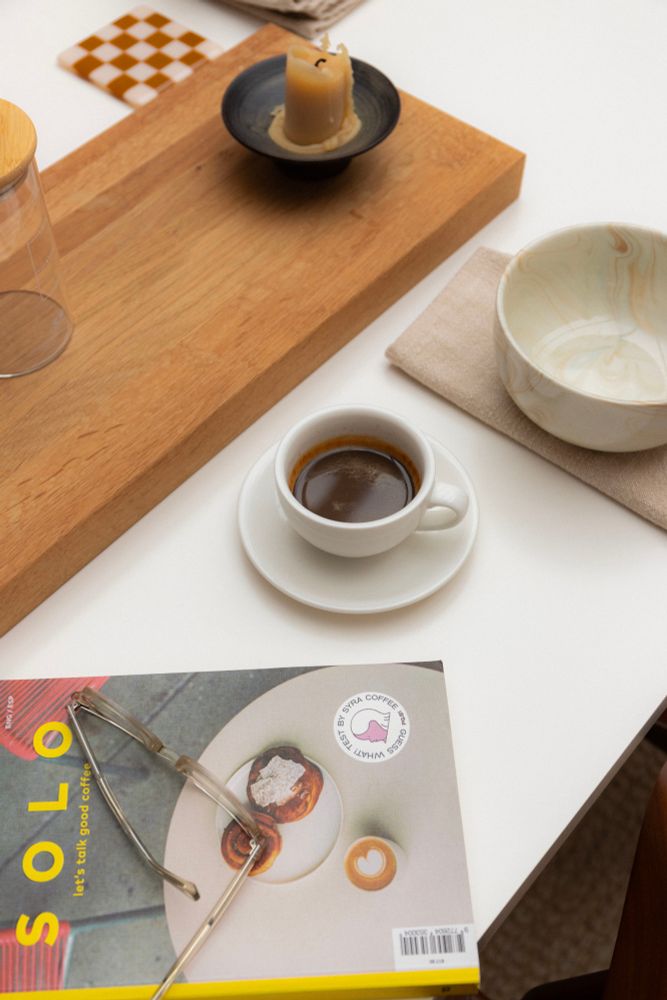 Espresso on table in between a candle and magazine titled SOLO