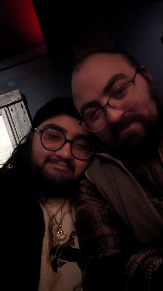 Two bearded men wearing glasses snuggled up smiling together for a photo