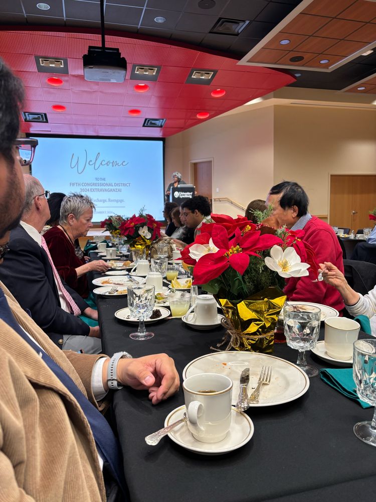 A table full of attendees listen to remarks while dining.
