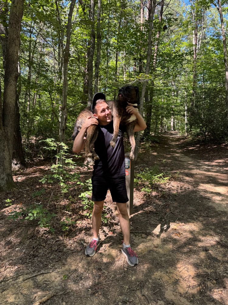 Mike on wooded trail with Jo (big black dog) resting on his shoulders