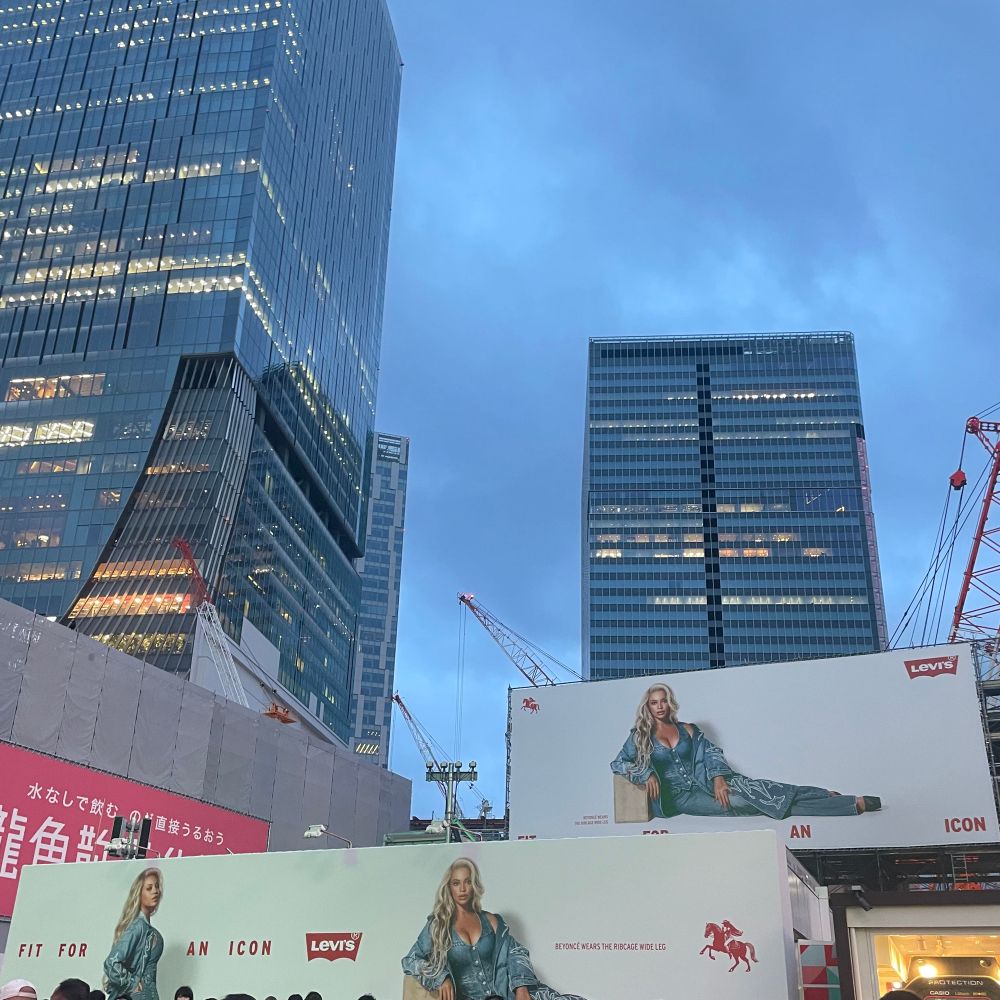 高層ビルの手前、渋谷ハチ公前付近に大きなリーバイスのビヨンセコラボ広告が掲げられている。白い背景に、小さくシンプルな赤いロゴとともに計3人の大きなビヨンセが描かれている。