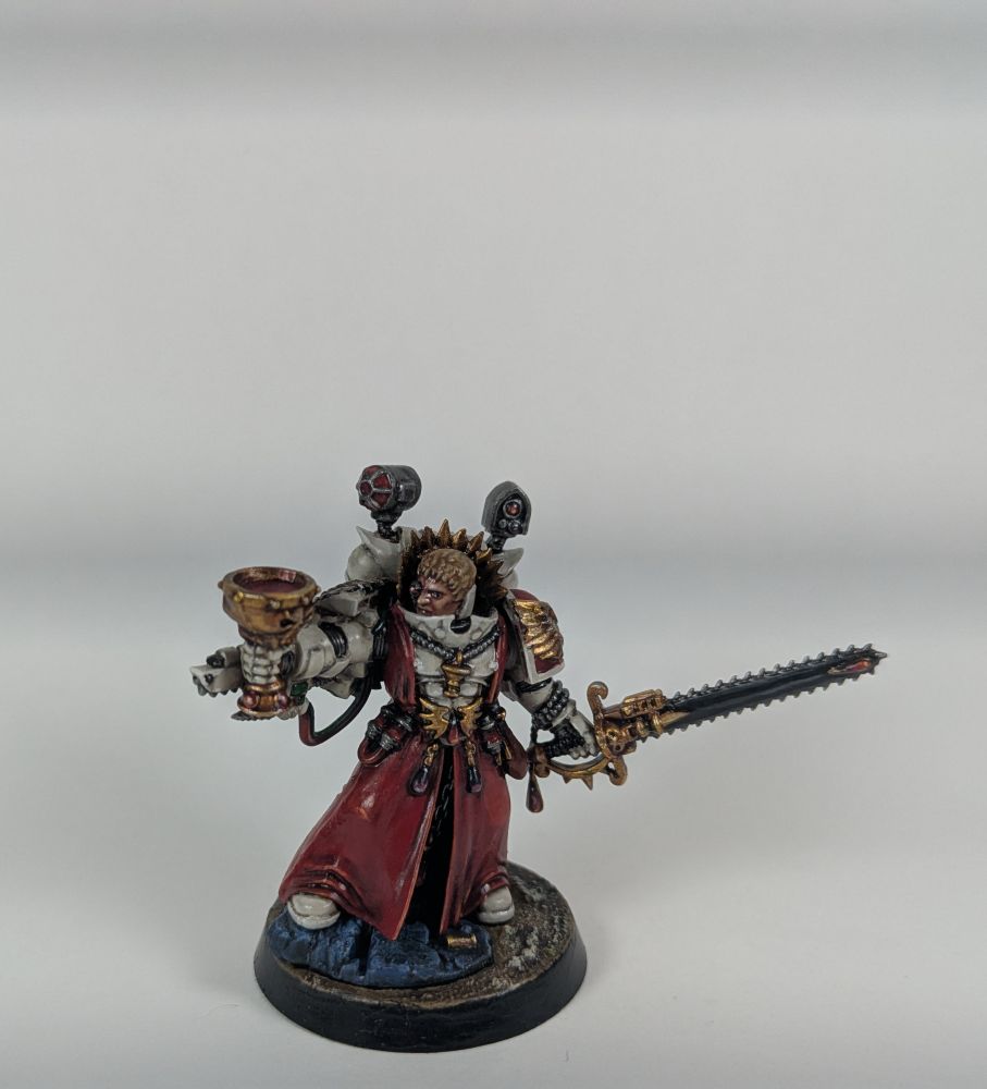 Sacerdote Sangriento, médico de los Ángeles Sangrientos, lleva un cáliz de bronce con diseños de calavera lleno de sangre en una mano y en la otra una espada sierra. Se distingue por su armadura finamente decorada en tonos blancos y sobrevesta y faldones que cubren sus piernas rojos.