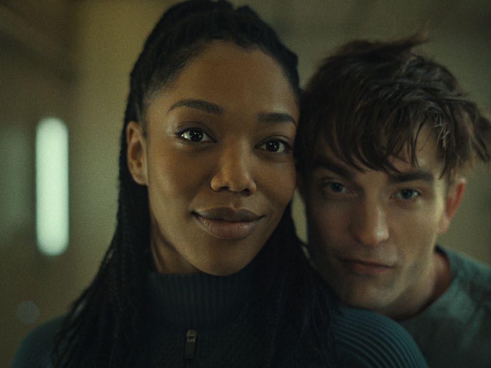 Photo from Little White Lies, Naomi Ackie, glowing black woman with tons of charisma, smarmy cute white boy Robert Pattinson resting his wee head of her shoulder