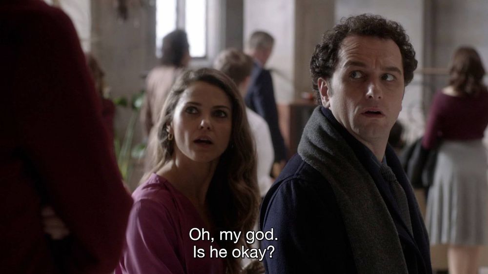 Elizabeth and Philip Jennings from The Americans. They are standing next to each other, both turned to look at someone behind them, and Elizabeth is saying oh my god. Is he okay?