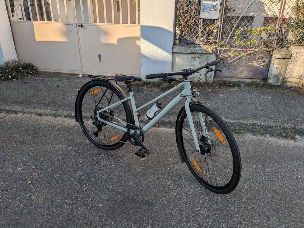 Photo d'un vélo VTC posé devant un portail. Il est coloré en un vert pistache subtil.