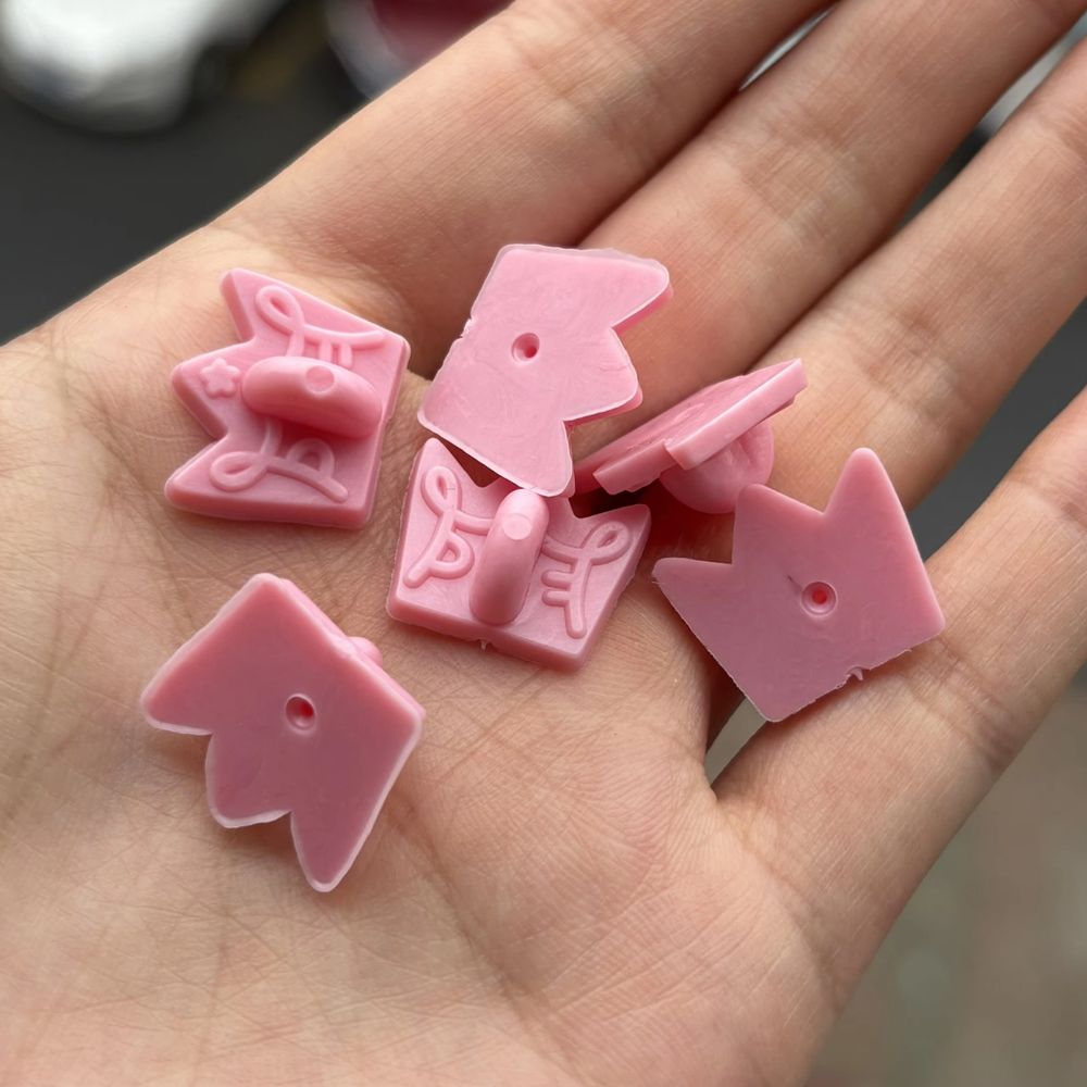 Image of pink rubber pin backings that are crown shaped with the Princefizz Art Logo embossed on them.