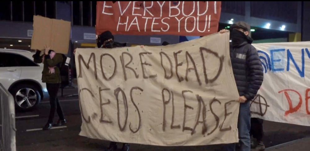 People in NYC holding banners during a CEO Event at Ziegfeld Ballroom that read "everybody hates you" and "more dead CEOS please"