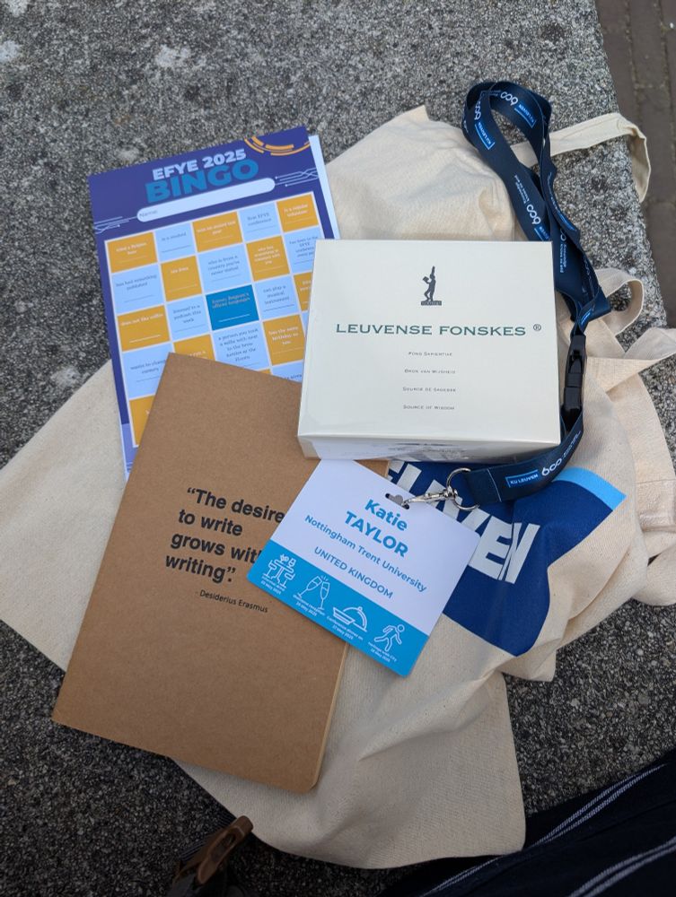 A photo of a bag with a notebook, conference bingo card, and chocolates on it.

