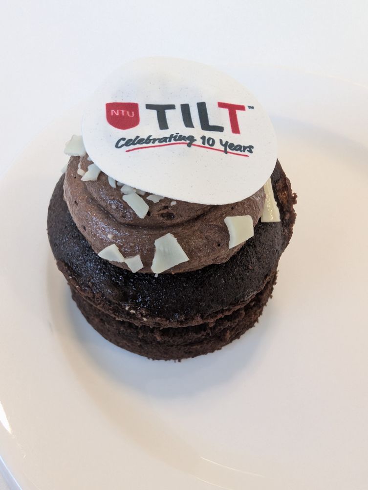 A small chocolate cake topped with chocolate icing and an edible paper top with the NTU TILT logo and Celebrating 10 years written on it.
