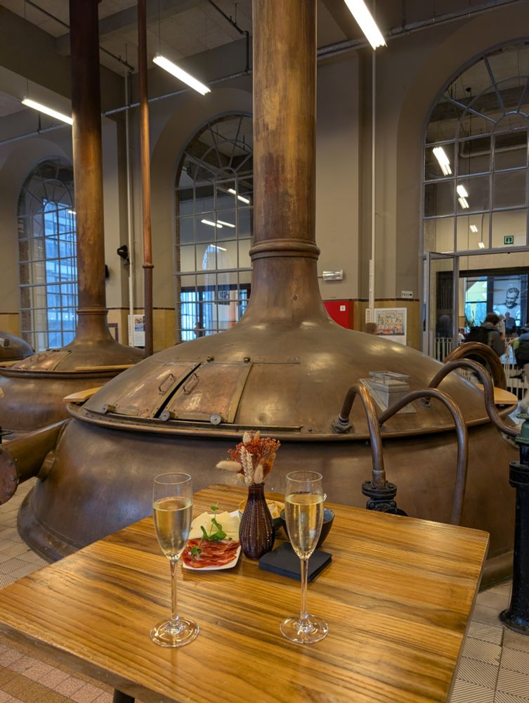 A photo of two champagne glasses on a table in front of an old brewers tank.
