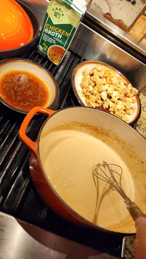 A stove top of chicken broth, chicken, andouille sausage, and a roux that is currently in progress 