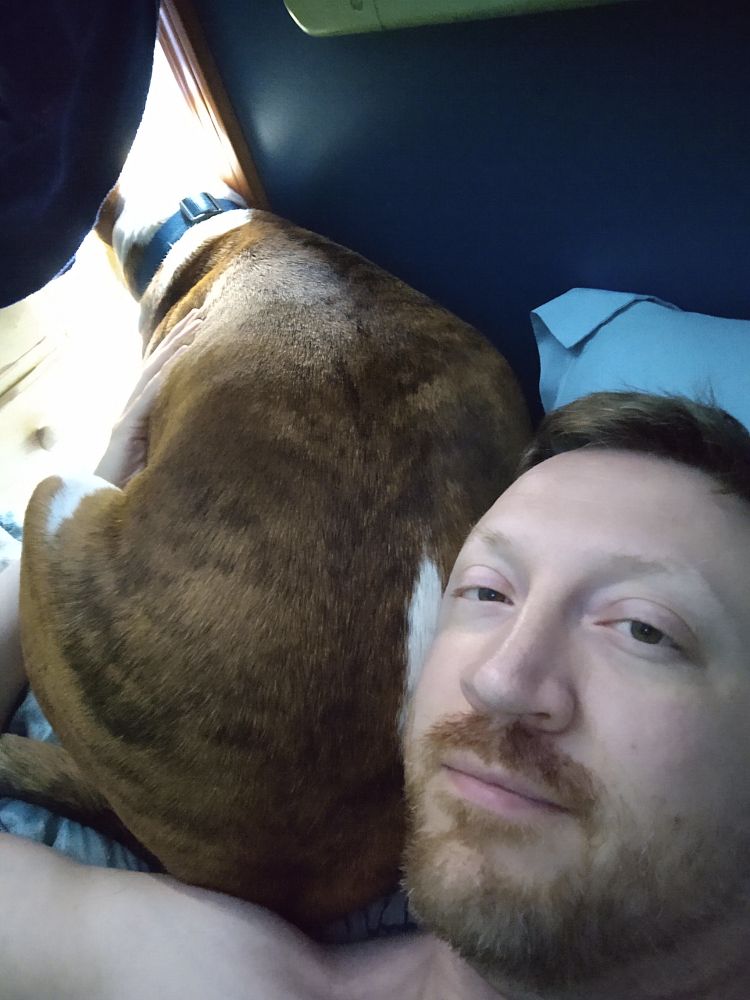 And man lying in bed while a dog is snuggled next to him