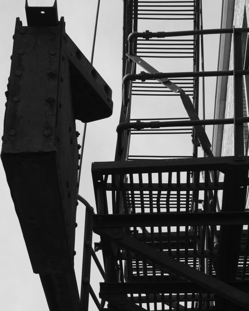 A shot of a fire escape and its counter weight. It’s a tight almost claustrophobic view. 