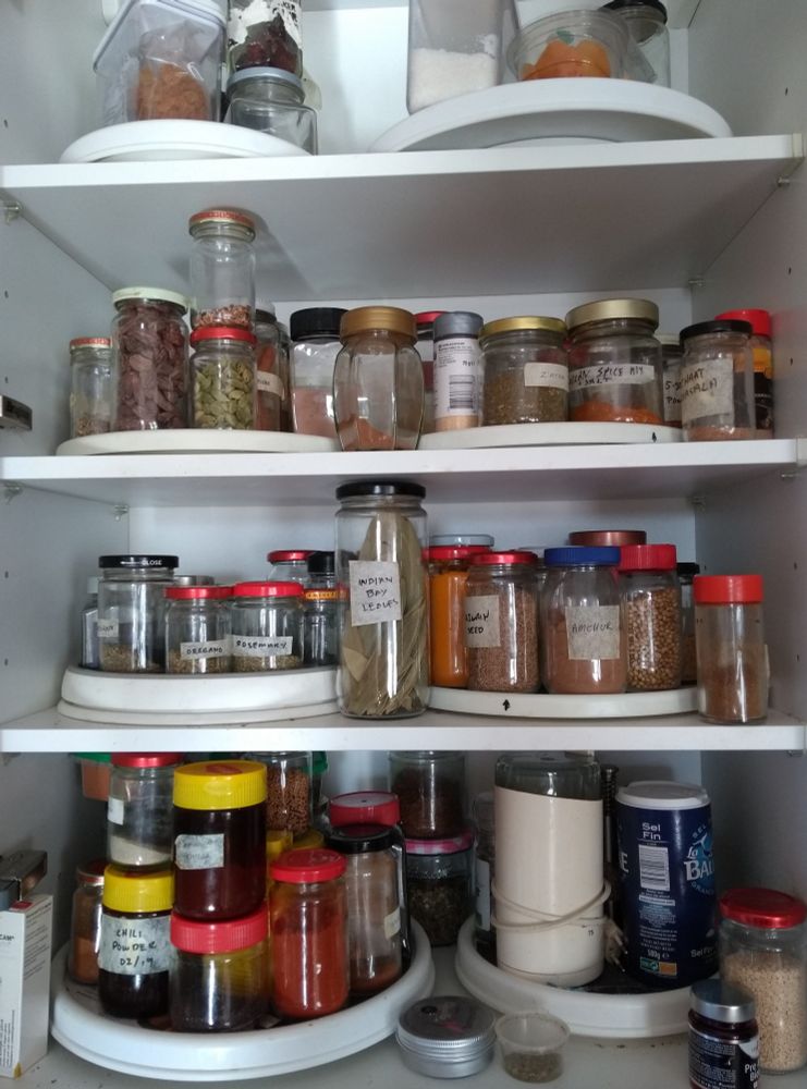 Open kitchen cupboard with four shelves, each holding 2 turntables containing miscellaneous jars of spices, plus a coffee grinder used only for grinding spices.