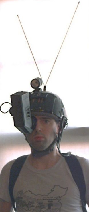 A man wearing a helmet with a huge antenna, and a vertical CRT display covering one of the man's eyes.