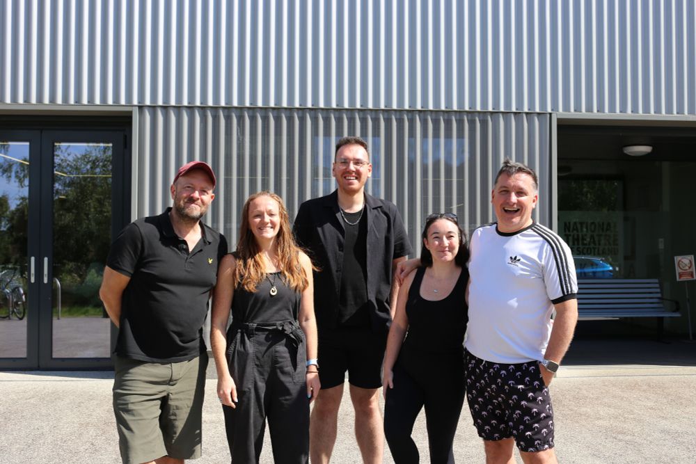 Five people are stood outside a grey steel building, smiling at the camera. 
