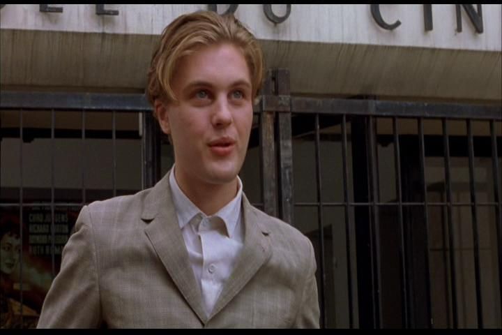 Actor Michael Pitt is dressed in a white shirt with a gray jacket on. He has medium “90s hair”