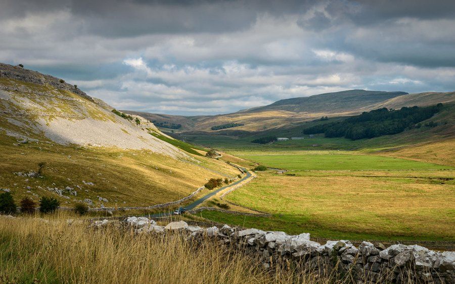 Kingsdale, Yorkshire Dales NP by YorkshireLass MaureenPlatts on X (posted with permission). A long and winding road flanked by green fields, rocks, and mountains.