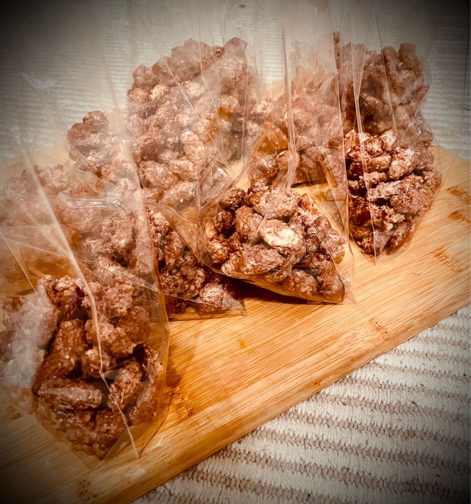 Zu sehen sind acht Tüten mit gebrannten Mandeln. Die Tüten stehen auf einem Holzbrett.