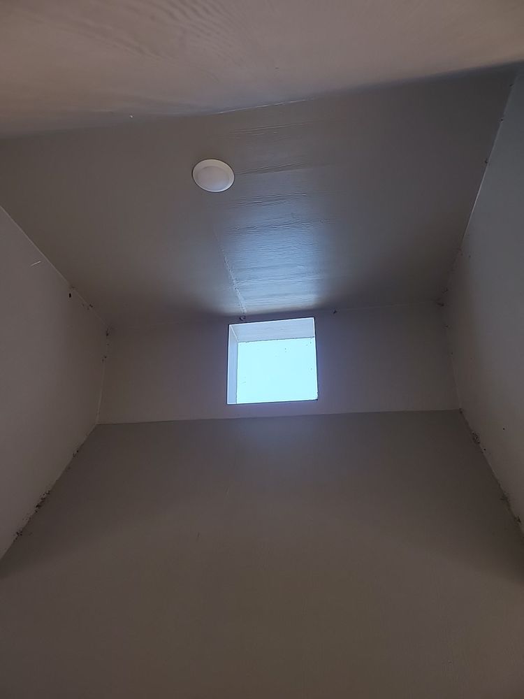 A sky light in a dark room. It is small, square, and illuminates the wall around it in light blue.