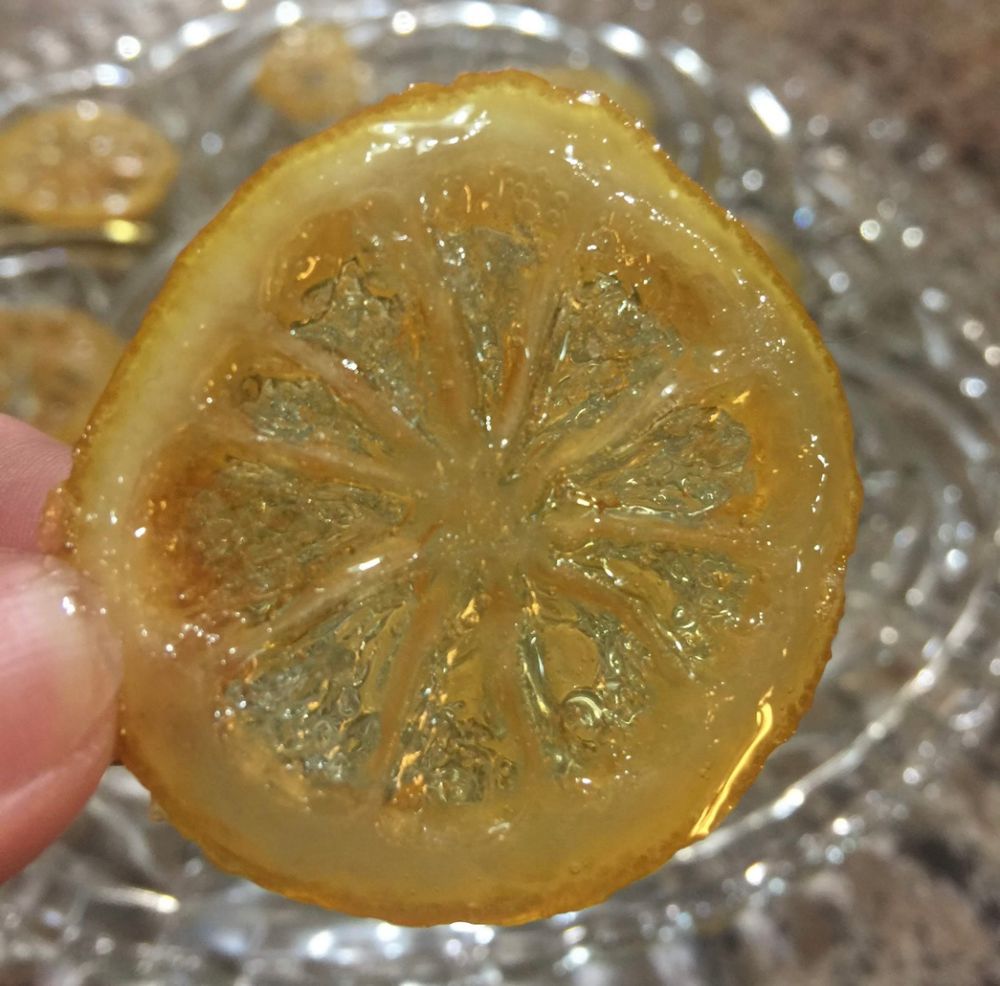 A candied lemon wheel in foreground with a glass platter of candied lemon wheels behind it 