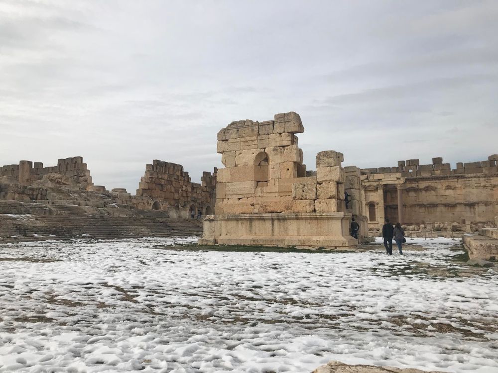 large open area within a ruin temple complex. there is a dusting of snow on the ground and in the middle is the remnants of a large stone square building.