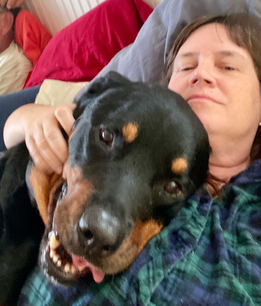 Me, lying on a bed, with a great big doofus rottweiler named Koda snuggled up to me. His head is on my chest and he's looking straight into the camera with a big smile and his tongue hanging out. 